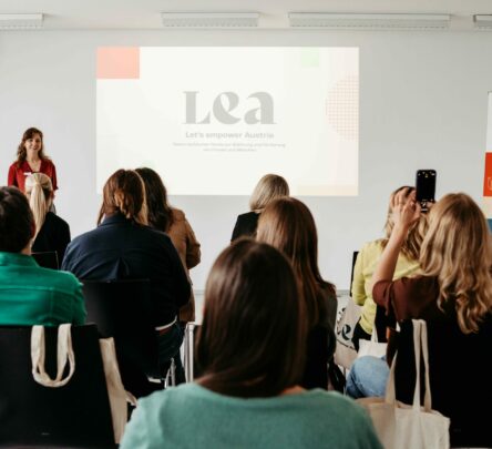 Eine stehende Frau hält eine Präsentation vor einer Gruppe sitzender Frauen.